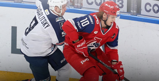 На изображении два хоккеиста соперничают за шайбу. Один в белой форме, другой в красной. Они находятся на льду возле борта, в спортивной арене. Видны логотипы и номера игроков на форме